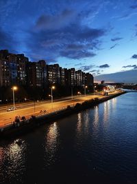 River by illuminated buildings against sky at dusk