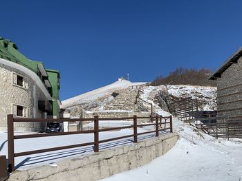 Snow covered houses by mountains against clear blue sky