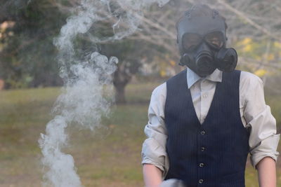 Teenage boy wearing gas mask while standing against trees