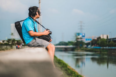 Side view of man photographing by lake against sky