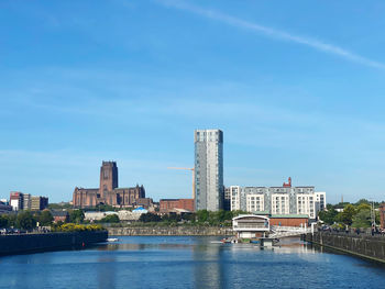 View of buildings by river against blue sky