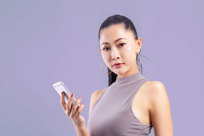 Portrait of young woman using smart phone against gray background