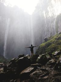 Man standing on rock against waterfall