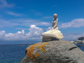 Statue on rock by sea against blue sky