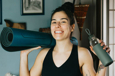 Portrait of smiling woman holding exercise mat at home