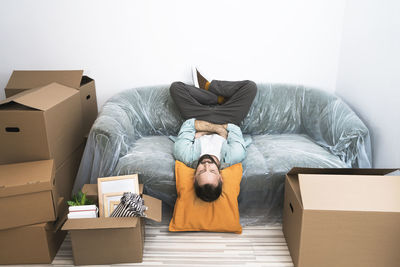 Adult man laying on sofa upside down in lotus position while moving in new house.