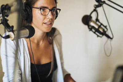 Radio podcast concept - female radio host speaking in microphone in podcasting studio