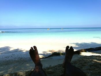 Low section of person on beach against clear blue sky