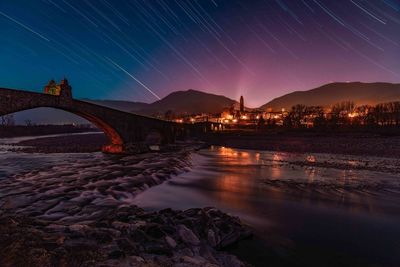 Illuminated bridge over river against sky at night