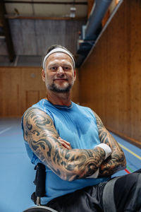 Portrait of confident male athlete sitting on wheelchair with arms crossed at sports court