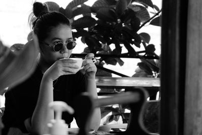 Portrait of young woman holding coffee while sitting on window