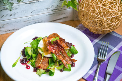 Poached egg on toast with fried bacon, cranberry sauce, and corn salad