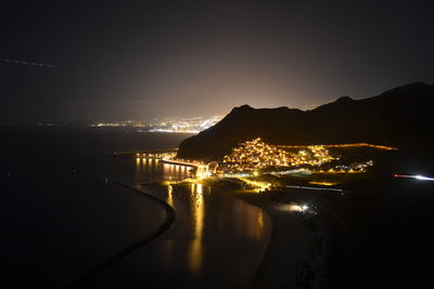 Illuminated city by sea against sky at night