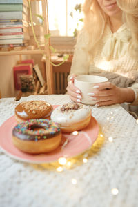 Midsection of young woman holding coffee cup by donuts