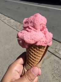 Hand holding ice cream cone with pink ice cream 