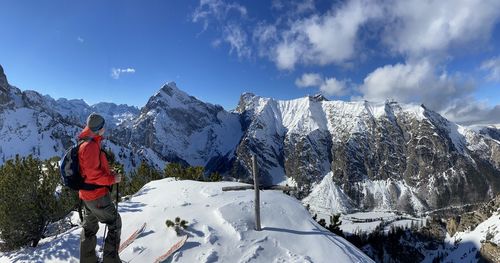 Rear view of man standing on snowcapped mountain against sky