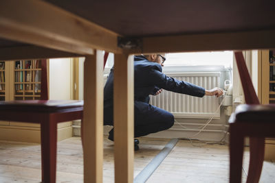 Low section of lawyer charging phone by radiator with table in foreground at library