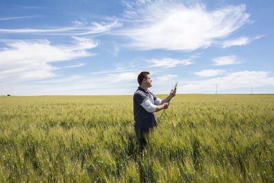 Rear view of young woman with arms outstretched on field against sky