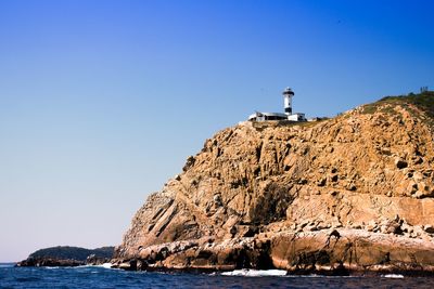 Lighthouse on cliff by sea against clear blue sky