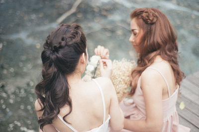 High angle view of young friends making tiara while sitting on jetty