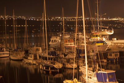 Boats moored in illuminated harbor against clear sky at night