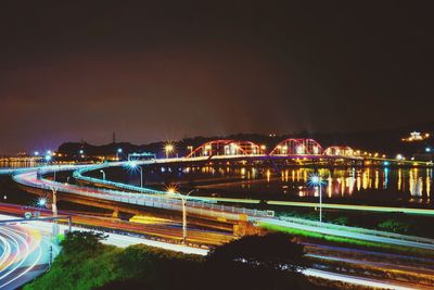 Light trails on bridge in city against sky at night