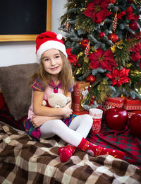 Portrait of smiling girl sitting on christmas tree