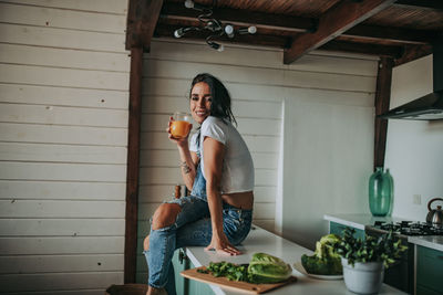 Woman drinking juice while sitting in kitchen counter