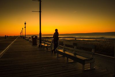 Silhouette woman standing on pier against clear sky during sunset