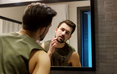 Reflection of young man on mirror in bathroom