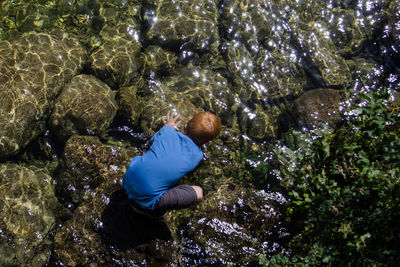 Directly above shot of boy crouching on rocks in river
