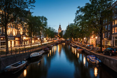 Boats moored at canal amidst illuminated buildings