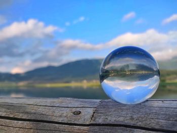 Close-up of water ball on wood against sky