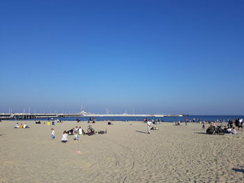 Group of people at beach against clear blue sky