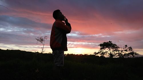 Silhouette man standing on field against sky during sunset