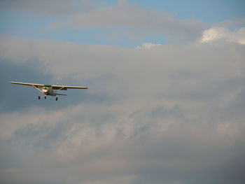 Low angle view of airplane flying against cloudy sky