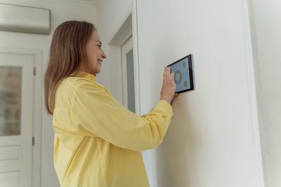 Smiling woman using tablet pc mounted on white wall at home