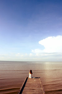 Rear view of woman sitting on pier over sea at beach