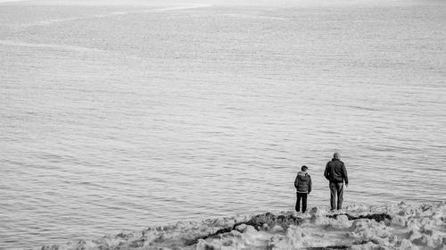 Rear view of father and son standing on cliff in front of sea