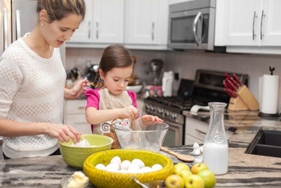 Cute girl with mother preparing food in kitchen