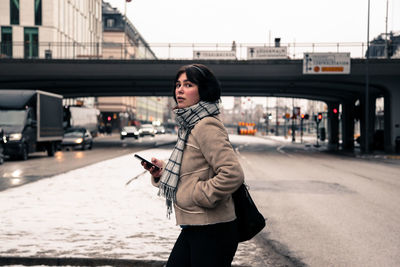 Young woman using phone while standing on bridge in city