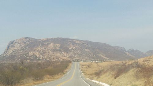 Empty road by mountains against clear sky