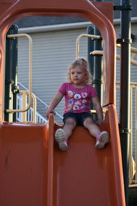 Cute girl sitting on slide in playground