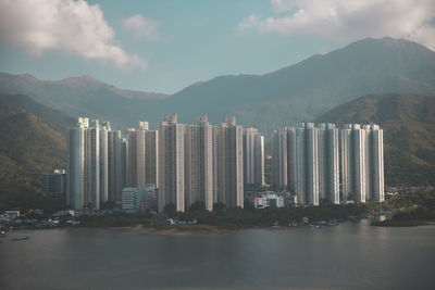 City by river and mountains against sky