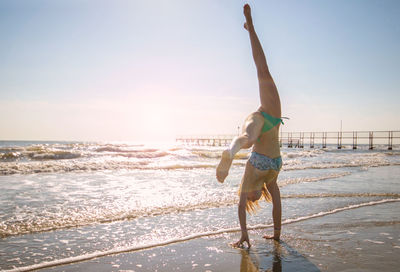 Full length of woman doing handstand at beach against sky