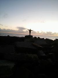 Man on rock against sky during sunset