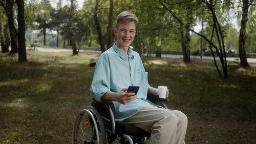 Portrait of smiling young man holding mobile phone sitting on wheelchair