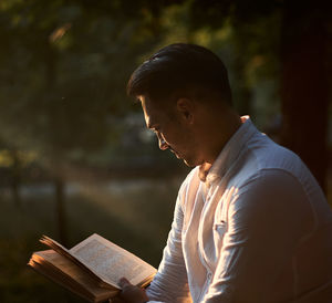 Side view of young man reading book