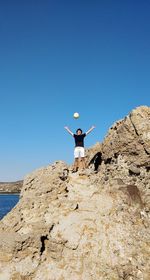 Man playing with ball on rock formation against clear blue sky