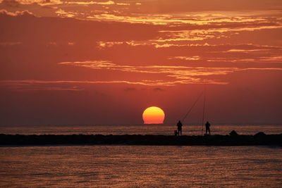 The sun appears among the fishermen on the breakwater